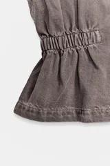 Chaleco de denim con cuello subido y manga sisa. Presenta cintura elástica con frunces laterales, cierre frontal con botones a presión y cremallera oculta.