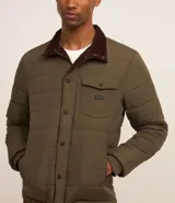 Campera puffer negra con cuello alto, cierre frontal con botones a presión, bolsillos laterales y un bolsillo cargo en el pecho. Presenta un diseño acolchado y forro interior suave.