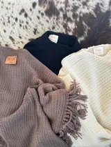 Poncho tejido en lana merino color marrón, con diseño de punto acanalado y terminación con flecos en el borde inferior. Incluye una pequeña etiqueta de cuero en la parte posterior.