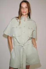 Mono corto de Zara Woman Collection color verde menta, confeccionado en mezcla de algodón y lino. Presenta cuello solapa, manga corta, cierre frontal con botones, bolsillos de plastrón con solapa en el pecho y cintura ajustable con lazo.