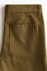 Pantalón de sarga de algodón verde militar, con piernas rectas y tiro medio. Presenta cierre con botón, bolsillos delanteros de parche conectados a las trabillas y bolsillos traseros también de parche.