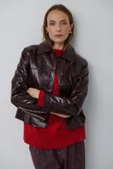 Chaqueta de efecto cuero brillante con acabado charol, cuello con solapas de piel sintética, cierre frontal con botones y bolsillos laterales.