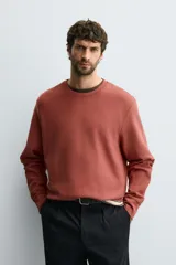 Sudadera de algodón color terracota, con cuello redondo, manga larga y puños y bajo acanalados. Presenta un efecto lavado que le da un aspecto desgastado.