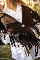 Chall de gamuza natural con diseño de flecos largos y pins decorativos en la parte frontal, estilo western.