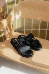 Sandalias tipo birkenstock de cuero negro, con base anatómica, dos tiras superiores ajustables con hebilla metálica y combinación de texturas en cuero liso y gamuzado.