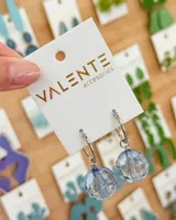 Aros tipo argolla de acero con dije colgante de esfera de cristal facetado en color celeste traslúcido.