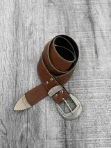 Cinto marrón de cuero sintético con hebilla metálica plateada con diseño labrado y puntera metálica plateada.