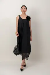 Vestido midi negro de gasa con escote redondo fruncido y detalle de aplicación de flor en el hombro. Presenta silueta fluida y ligera.