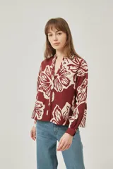 Camisa de poliéster con estampado floral en tonos bordó y crema, de corte holgado, cuello mao y cierre frontal con botones.