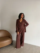 Conjunto de tres piezas compuesto por blazer, chaleco abotonado y pantalón de corte sastre con piernas anchas. Todas las prendas presentan un diseño a rayas verticales finas en color marrón.