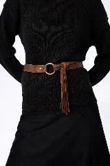 Faja de cuero marrón con diseño de argolla metálica central y detalle de flecos de gamuza colgantes. Presenta un cierre con broche a presión y una estructura que combina napa lisa y gamuza.