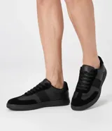 Championes urbanos para hombre en color negro, con diseño monocromático de perfil bajo. Combinan inserciones de material sintético y textura tipo gamuza en la puntera y laterales, con cierre de cordones al tono.