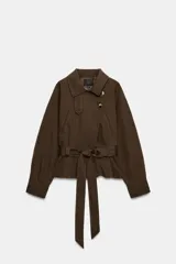 Cazadora trench corta color marrón, confeccionada en mezcla de algodón, con cuello solapa, cierre cruzado con botones, bolsillos de vivo en el delantero y cinturón ajustable del mismo tejido.
