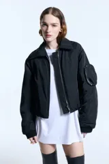 Campera tipo bomber de nylon con ligero relleno, corte cropped y ajuste recto. Presenta cuello camisero, cierre frontal metálico, puños de ribb y bolsillos frontales con tapa. Incluye un bolsillo decorativo con cierre en la manga y bordado a tono en el frente.