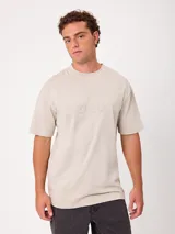Remera de algodón color beige con efecto de lavado ácido, corte holgado, cuello redondo ancho y diseño minimalista con bordado sutil en el pecho.