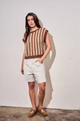 Chaleco de punto sin mangas con diseño de rayas verticales en tonos marrón, blanco y mostaza. Presenta cuello redondo y terminaciones acanaladas en color marrón sólido.