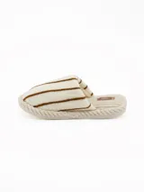 Pantuflas abiertas de estilo mule, con capellada de peluche color crema con rayas negras horizontales y plantilla de pana acanalada en tono beige.