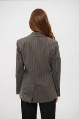 Blazer de mujer gris oscuro con finas rayas verticales blancas, de corte entallado y solapas clásicas. Se lleva abierto sobre un top blanco de cuello alto.