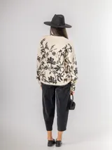 Sweater de punto con calce oversized, fondo color crudo y diseño estampado de flores en color negro. Presenta cuello redondo y mangas largas.