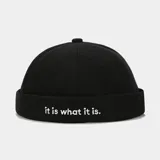 Gorro estilo docker (sin visera), color negro, con borde doblado y bordado frontal en blanco que dice "it is what it is".