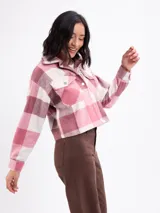 Sobrecamisa de corte cropped con diseño a cuadros en tonos rosa y beige. Presenta cuello clásico, cierre frontal con botones metálicos, mangas largas con puños abotonados y dos bolsillos frontales con solapa.