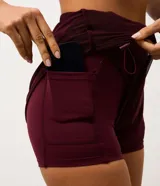 Bermuda deportiva femenina modelo runner, color bordó, con short interno incorporado. Presenta cintura elástica con cordón de ajuste y laterales con cordones ajustables. Confeccionada en tejido de tul con tecnología dry para mayor transpirabilidad.