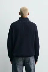 Jersey de punto perlado con cuello perkins y cierre frontal de cremallera. Presenta un corte regular fit, manga larga y acabados en rib en puños y bajo.