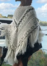 Ruana tejida artesanalmente en lana merino, con diseño de calados geométricos y terminación de flecos largos en el ruedo.