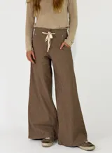 Pantalón de corte ancho y tiro medio, confeccionado en tela de textura rústica color marrón. Presenta cintura elástica con cordón de ajuste frontal, bolsillos laterales y costuras reforzadas en el ruedo.