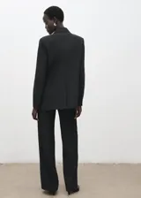 Pantalón de traje de tiro medio, color negro, de diseño recto y largo, con cierre frontal de cremallera, botón y ganchos ocultos con tapeta, y bolsillos laterales.