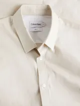 Camisa de manga larga color blanco hueso, de corte slim, con cuello tradicional y cierre frontal de botones.