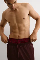 Pack de dos calzoncillos tipo boxer en tejido suave, con cintura elástica y bragueta de botones. Uno de ellos presenta un patrón a cuadros pequeños en tonos rojo y blanco, mientras que el otro cuenta con un diseño de cuadros tipo tartán en tonos rojo y negro.