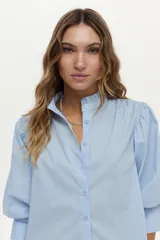 Camisa blanca de cuello mao con volados, mangas abullonadas y cierre frontal con botones.