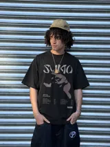Remera marrón oversize con efecto acid wash, corte amplio y mangas cortas. Presenta un estampado frontal en tonos celestes y grises con la inscripción 'Sumo', una ilustración de un luchador de sumo y detalles tipográficos alusivos a un álbum musical.