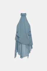 Top halter de cuello subido y hombros descubiertos, confeccionado en tejido fluido con diseño asimétrico y bajo con volantes. Cuenta con cierre en el cuello.