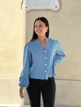 Camisa de jean celeste con cuello redondo, cierre frontal con botones y mangas largas abullonadas con puños ajustados.
