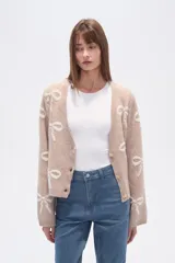 Cárdigan color beige con estampado de moños blancos, escote en V y cierre frontal con botones.