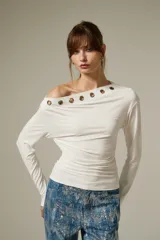 Remera de manga larga color blanco, confeccionada en viscosa, con diseño al cuerpo y cuello asimétrico decorado con ojales metálicos.