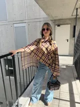 Poncho beige con estampado a cuadros en tonos marrón, negro y rojo, con diseño asimétrico y escote redondo.