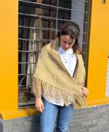 Ruana triangular de lana merino color tostado, tejida a mano con textura de punto y terminación de flecos en los bordes.