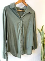 Camisa celeste de corte holgado, con cuello clásico, cierre frontal con botones, bolsillo en el pecho y mangas largas con puños abotonados.