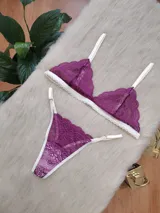Conjunto de lencería compuesto por un bralette triangular y una tanga, confeccionados en encaje color fucsia con terminaciones y breteles en color crema. El bralette presenta un diseño sin aros con bordes festoneados, mientras que la tanga cuenta con tiras laterales regulables.