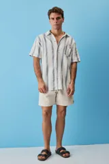 Camisa de manga corta a rayas verticales en tonos azul y blanco, con cuello camisero, cierre frontal de botones y un bolsillo en el pecho con etiqueta aplicada.