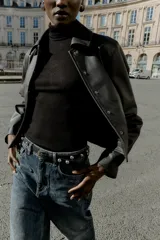 Cazadora corta negra de efecto piel, con cuello solapa, manga larga y cierre frontal con botones a presión ocultos. Incluye bolsillos delanteros de vivo con botón a presión y bajo con elástico en la espalda.