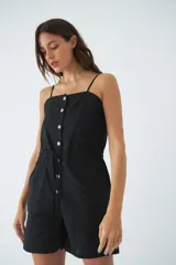 Monoprenda corta de color verde oliva, con tirantes finos ajustables, cierre frontal con botones y cintura elástica con cordón ajustable. Cuenta con bolsillos laterales.