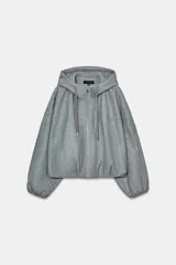 Chaqueta estilo bomber de corte oversize en color gris, confeccionada en tejido suave. Presenta capucha con cordones ajustables, cierre frontal con cremallera, mangas largas con puños elásticos y bajo con pliegues. Incluye bolsillos delanteros de vivo.