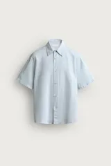 Camisa de manga corta color celeste, de corte regular fit, confeccionada en mezcla de algodón y lino. Presenta cuello camisero clásico y cierre frontal con botones.