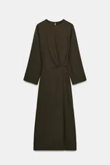 Vestido midi de Zara Woman Collection, color verde oscuro, con cuello redondo, manga larga y detalle de pliegues en el delantero. Presenta un corte recto con abertura frontal en el bajo y cierre lateral con cremallera oculta.