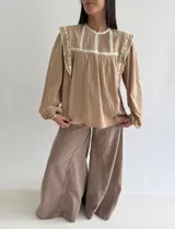 Blusa de algodón color beige con cuello redondo, mangas largas abullonadas con puños elásticos, detalles de puntilla y bordados florales en el frente.
