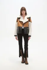 Chaqueta estilo aviador o biker, con paneles de color marrón (simil gamuza), negro (simil cuero acolchado) y blanco (simil borrego/sherpa). Presenta cuello solapa ancho forrado en blanco, detalles de hebillas negras en los hombros y cierres metálicos en la parte delantera.